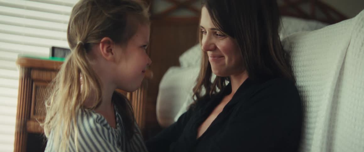 An affectionate mother cuddles with her young daughter, sharing tender kisses and smiles in a cozy bedroom