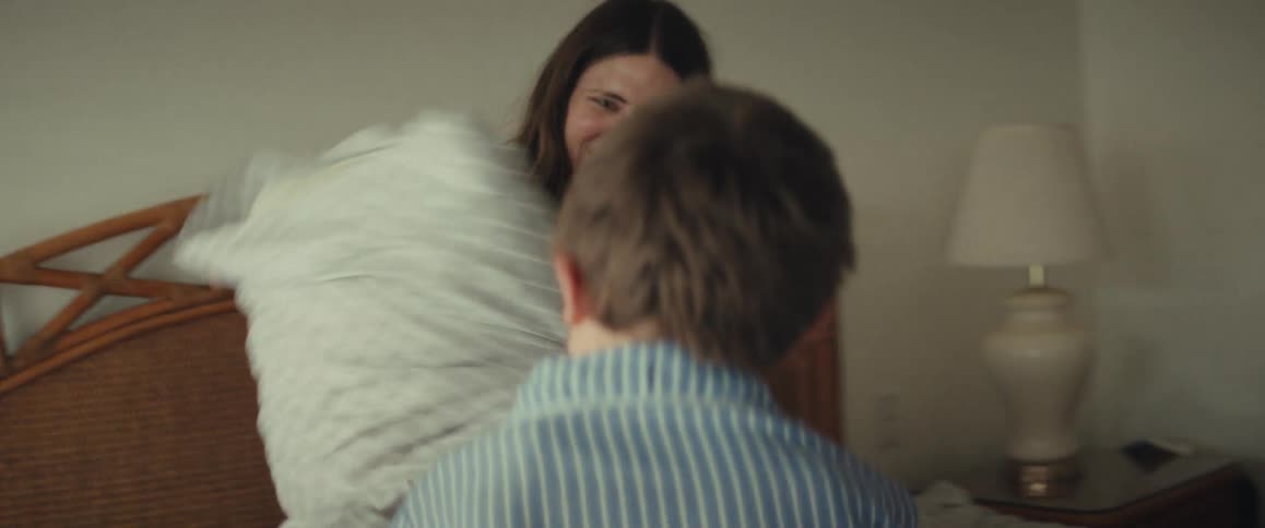 A young boy in pajamas has a fun pillow fight with his smiling mother on a bed in slow motion