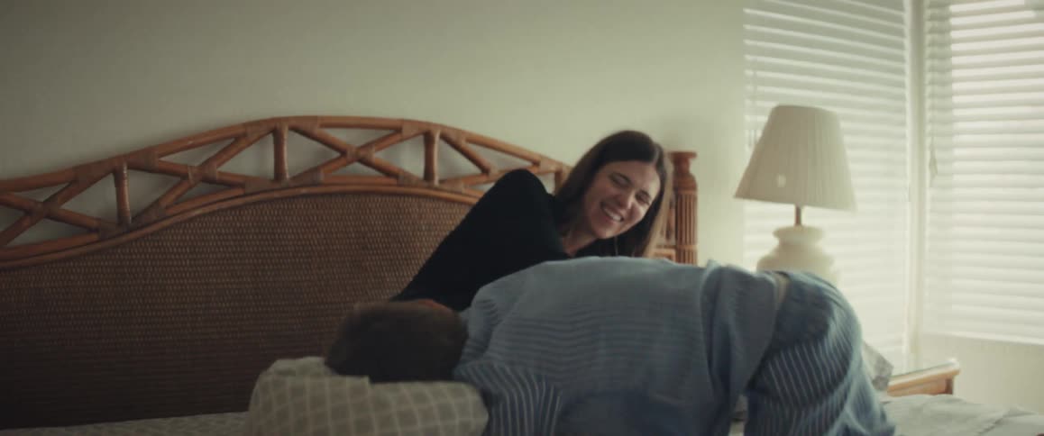 A joyful mother and her young son laugh and have a playful pillow fight in their pajamas on a bed in slow motion
