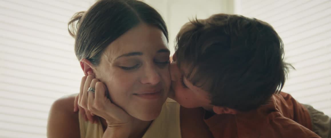 A young boy affectionately puts his arm around his mother and gives her a sweet kiss on the cheek