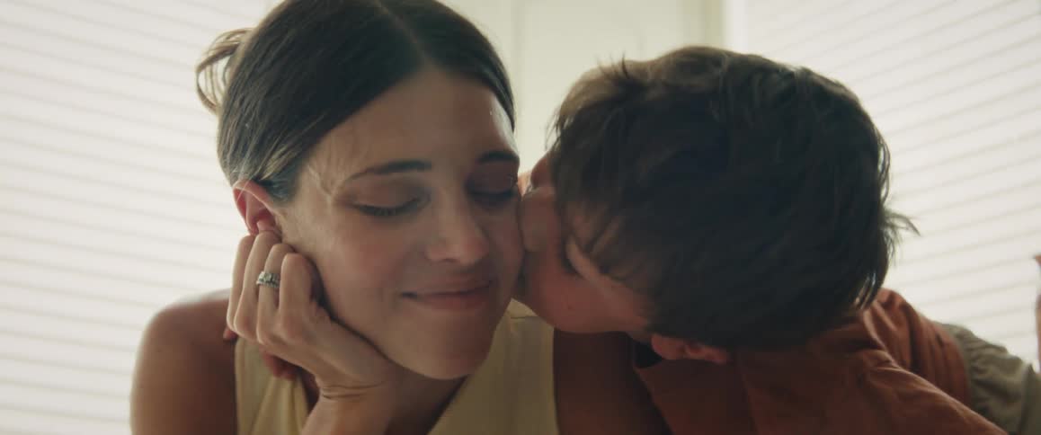 A young boy affectionately puts his arm around his mother and gives her a sweet kiss on the cheek