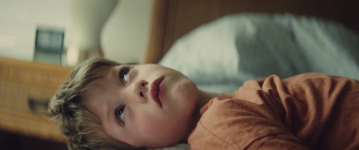 Close-up of a thoughtful young boy lying on his side in bed, daydreaming in the soft morning light