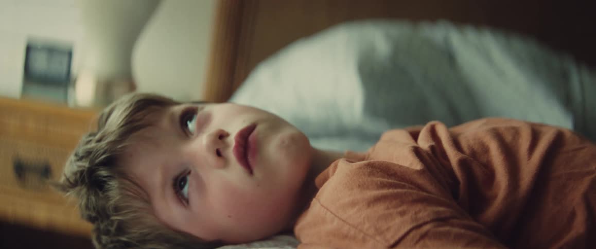 Close-up of a thoughtful young boy lying on his side in bed, daydreaming in the soft morning light