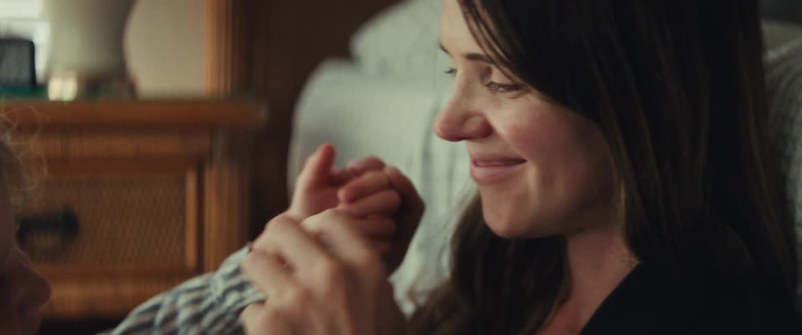 A loving mother gently kisses her smiling daughter's hand in a tender, intimate moment at home