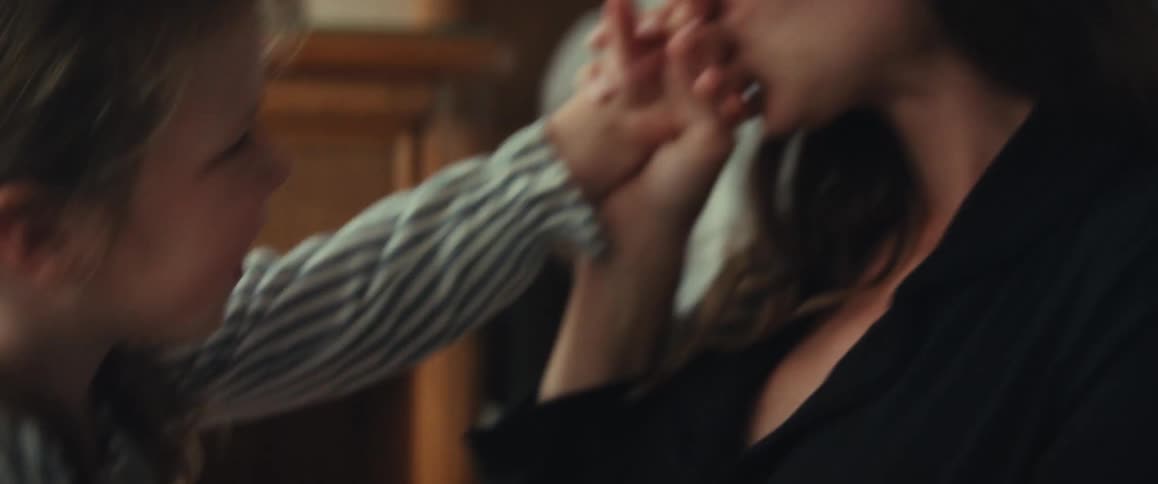 A loving mother gently kisses her smiling daughter's hand in a tender, intimate moment at home