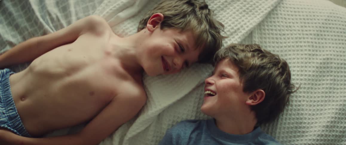Two young boys lie on a bed laughing and sharing a playful moment together