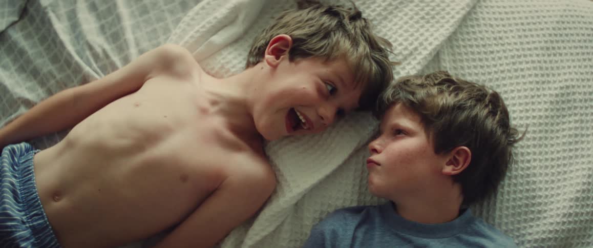 Two young boys lie on a bed laughing and sharing a playful moment together