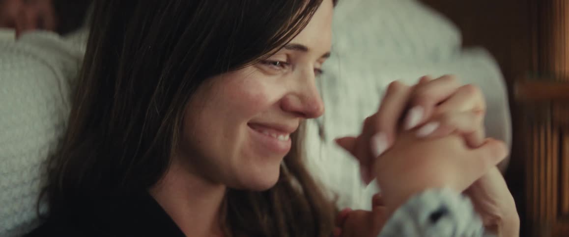 A loving mother playfully holds her young daughter's hands, smiling and sharing a tender moment together indoors