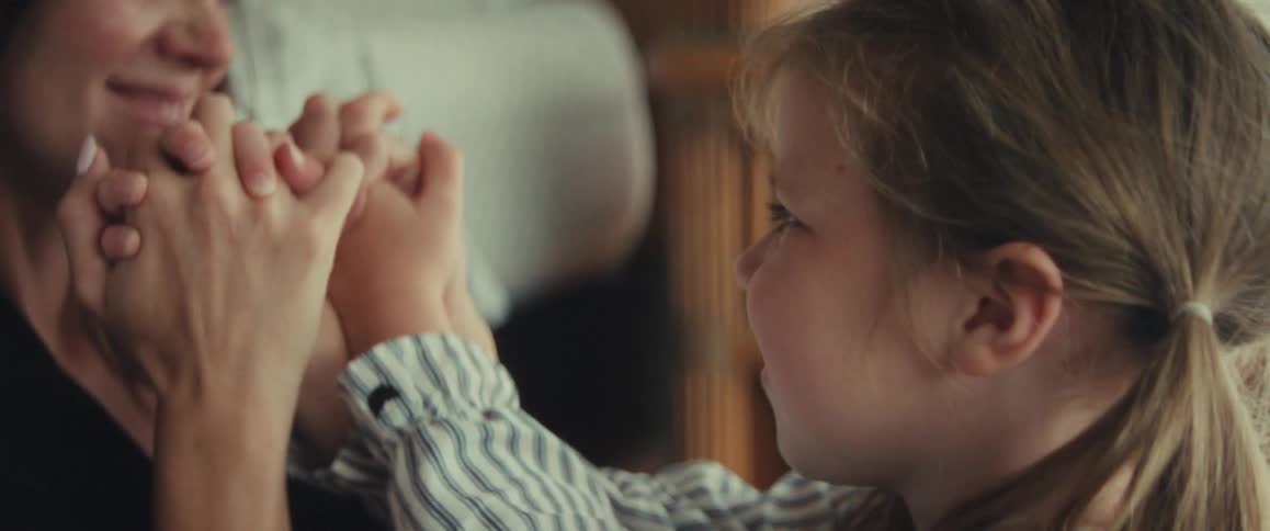 A loving mother playfully holds her young daughter's hands, smiling and sharing a tender moment together indoors