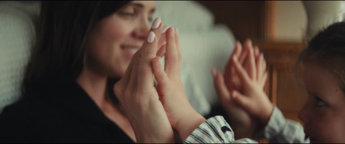 A tender close-up of a mother and her young child's hands playfully intertwining together indoors