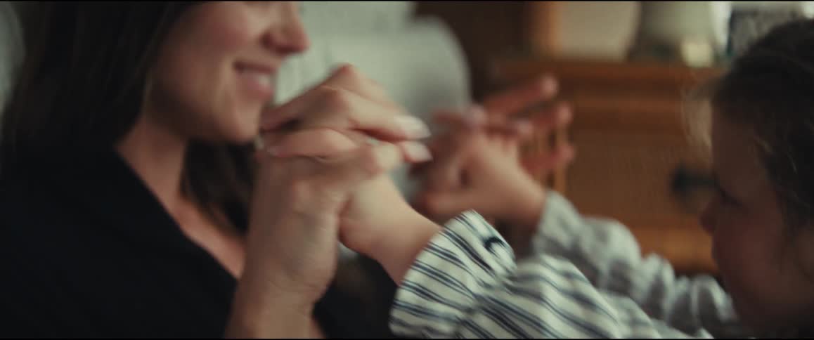 A tender close-up of a mother and her young child's hands playfully intertwining together indoors