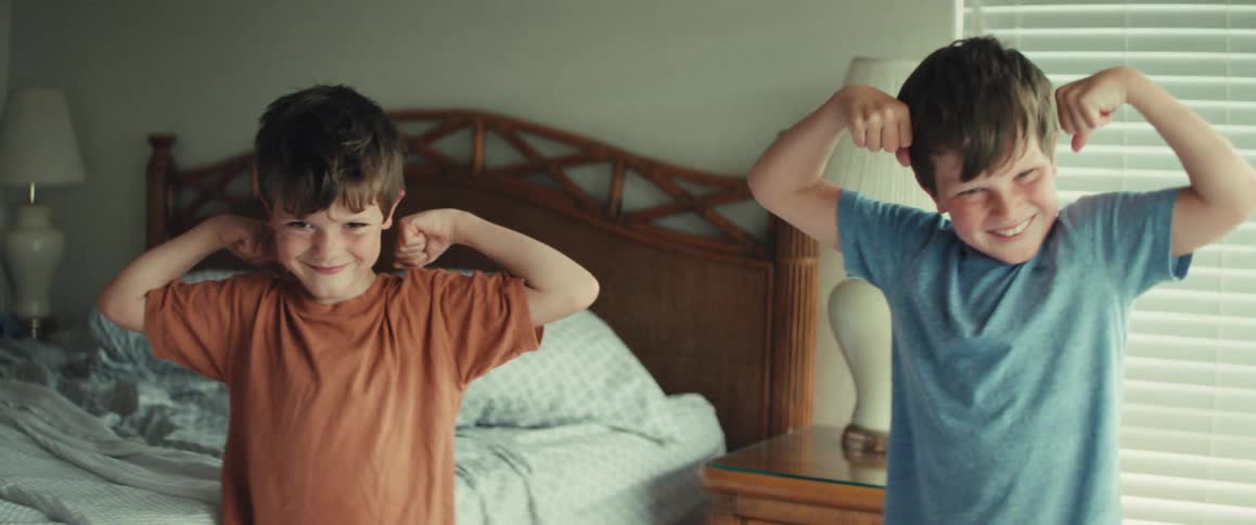 Two strong little boys happily show off their muscles while flexing in their bedroom