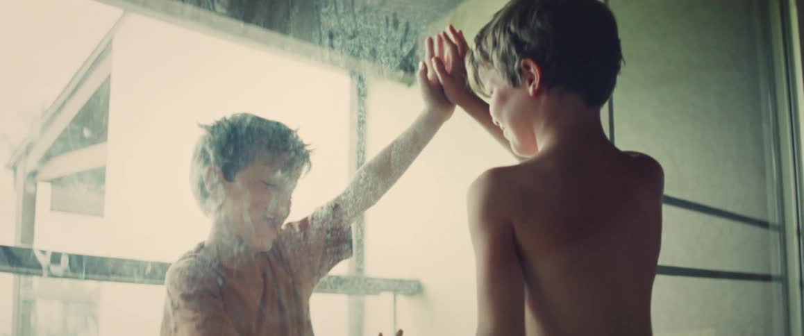 Young boy playfully presses hands against a foggy glass door indoors with warm natural light