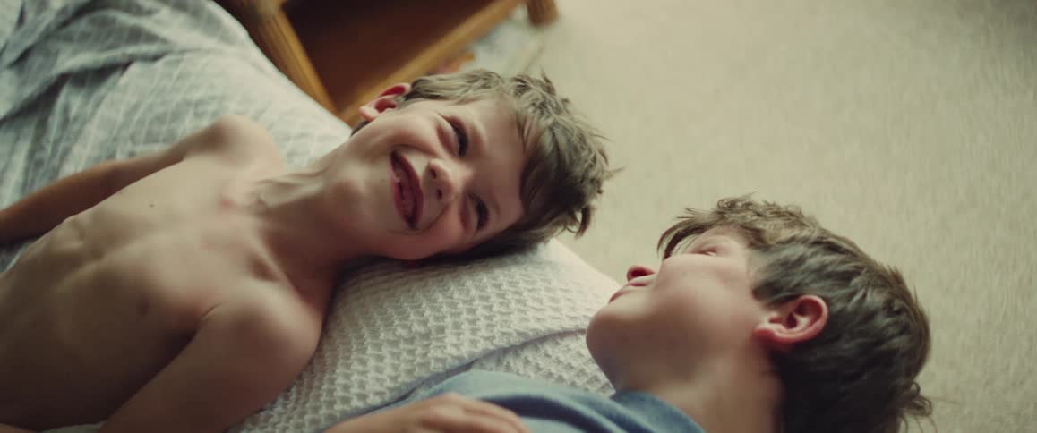 Two young boys smile and relax together on a bed in a cozy bedroom