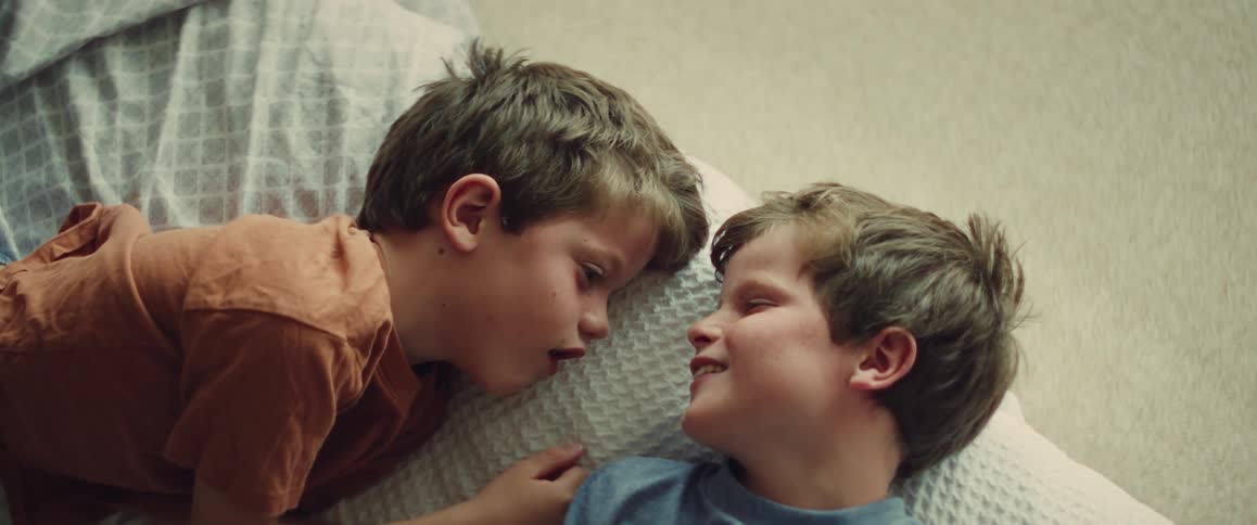 A heartwarming slow-motion shot captures two young brothers laughing and playfully tickling each other while lying on a bed