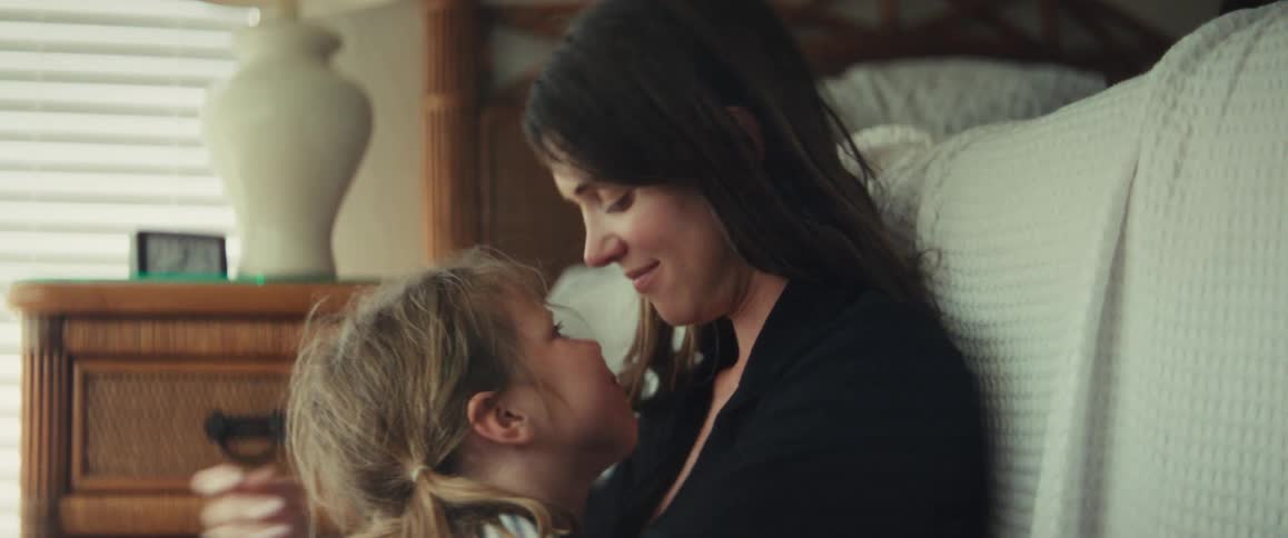 A loving mother and her young daughter share a tender moment, touching noses and hugging in a cozy bedroom