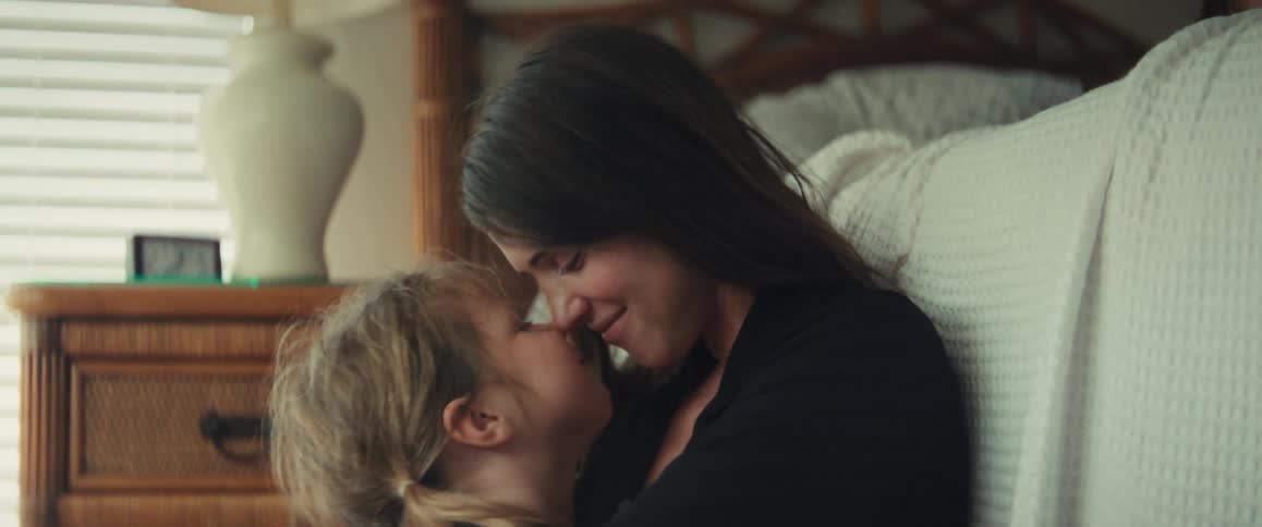A loving mother and her young daughter share a tender moment, touching noses and hugging in a cozy bedroom