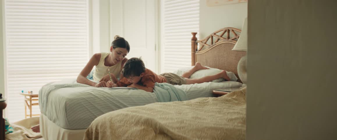 A loving mother and her young son share a quiet moment drawing together in a bright, sunlit bedroom