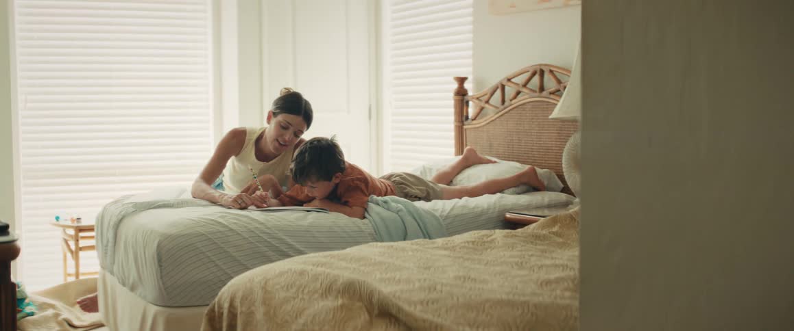 A loving mother and her young son share a quiet moment drawing together in a bright, sunlit bedroom
