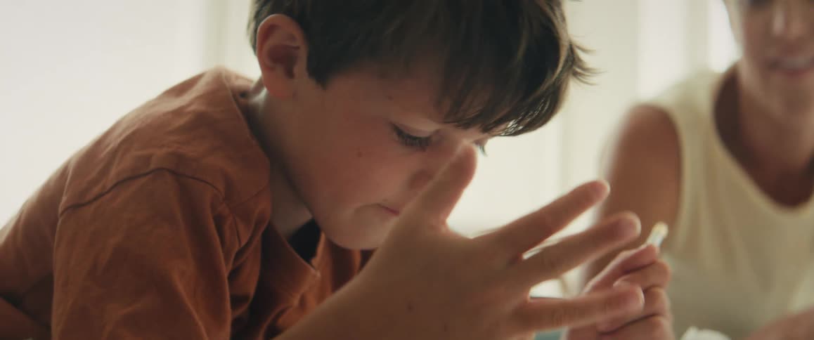 A schoolboy wearing an orange t-shirt concentrates deeply as he counts on his fingers to solve a math problem