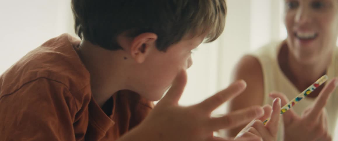 A schoolboy wearing an orange t-shirt concentrates deeply as he counts on his fingers to solve a math problem