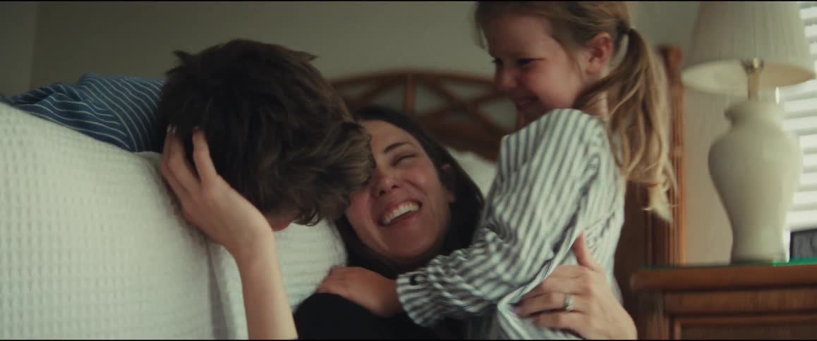 A happy mother laughs and smiles as her son and daughter shower her with hugs and kisses in a warm, inviting bedroom