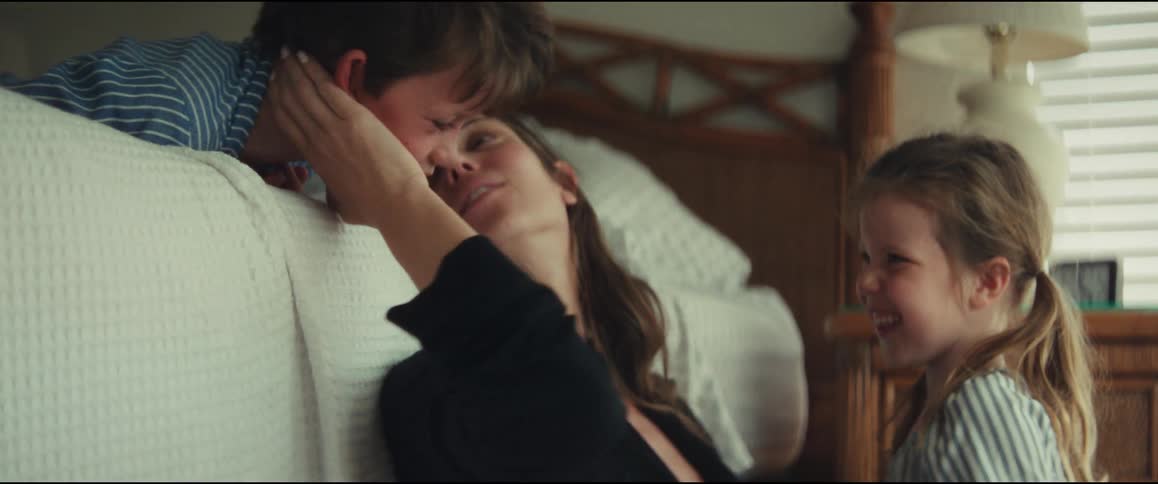 A happy mother laughs and smiles as her son and daughter shower her with hugs and kisses in a warm, inviting bedroom