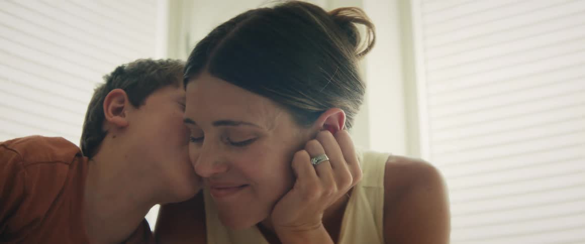 A young boy whispers in his mother's ear and gives her a kiss on the cheek during a tender moment at home