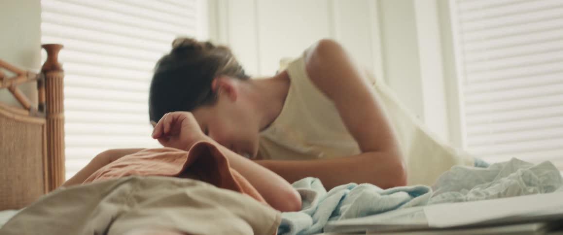 A joyful mother and her young son laugh and play together, sharing a loving and ticklish moment on a bed in a sunlit room
