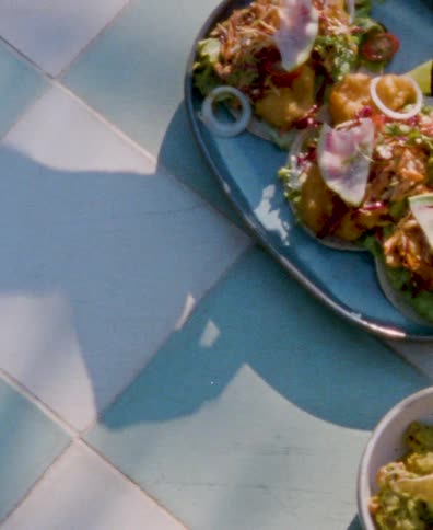 A sunny overhead shot of fresh tacos and guacamole served on a beautiful tiled table