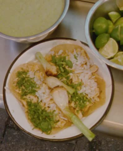 A top-down, close-up shot of a plate of authentic Mexican tacos garnished with cilantro and grilled spring onions, served with salsa and limes