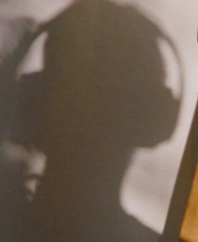 The shadow of a person wearing headphones is cast on a wall as they listen to music