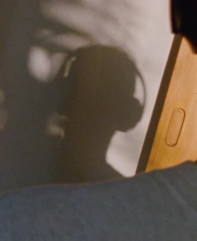 The silhouette of a person wearing headphones is cast on a wall as they listen to music in a sunlit room