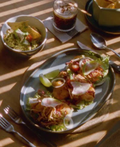 Gourmet tacos and guacamole sit on a wooden table, bathed in the warm, striped sunlight from a window