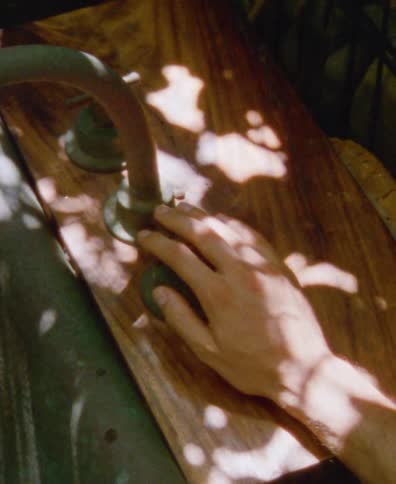 A hand turns the knob on a vintage wooden outdoor sink basked in dappled sunlight