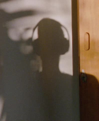 The grainy shadow of a person wearing headphones is cast on a wall as they listen to music