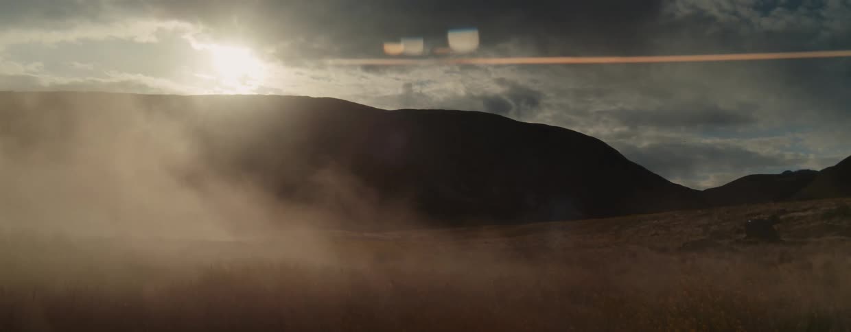 Mysterious fog rolls across a vast highland landscape as the bright sun shines through dramatic clouds