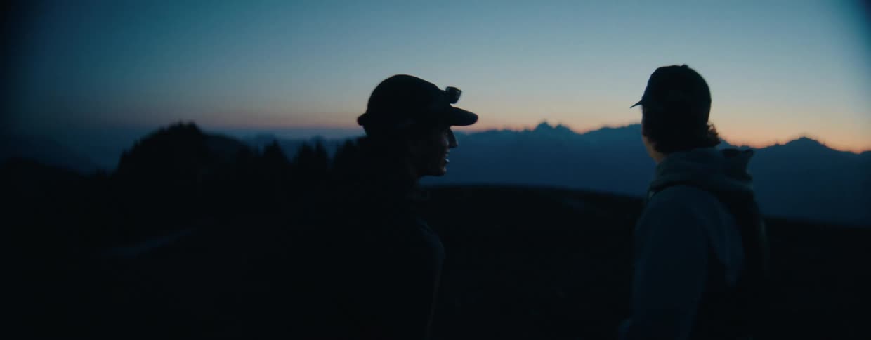 Two male hikers wearing headlamps greet each other with a fist bump before watching the beautiful mountain sunrise together