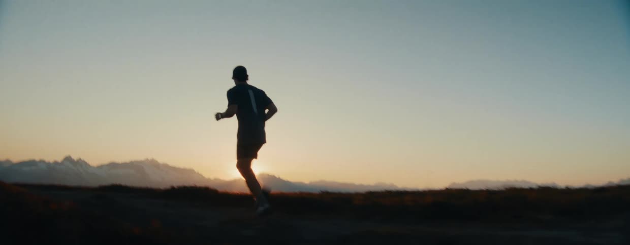 Slow motion silhouette of a man trail running on a mountain ridge during a beautiful golden sunset
