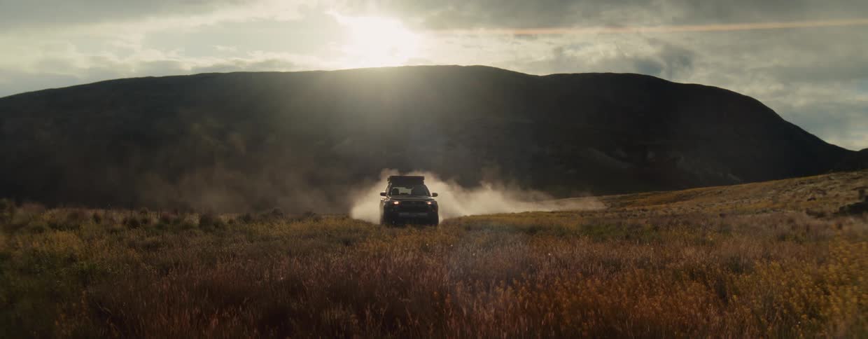 An overlanding SUV drives across a dusty landscape, silhouetted by the setting sun