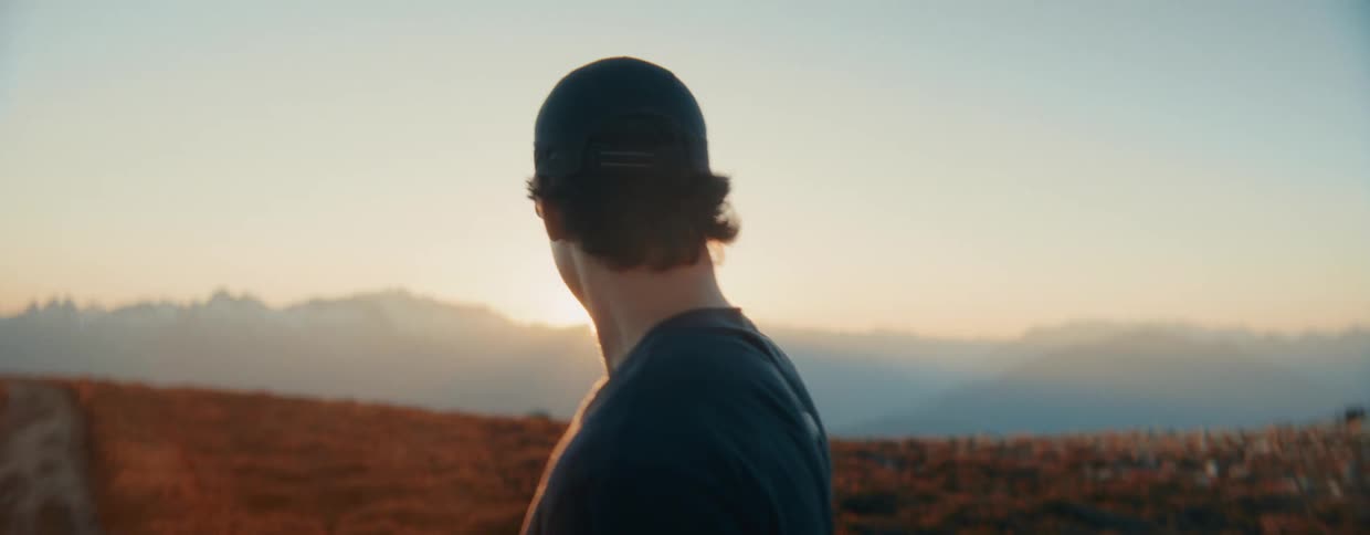 A young man lifts his head in slow motion and smiles, basking in the warm glow of a mountain sunrise
