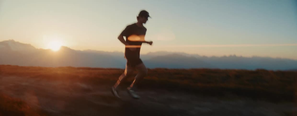 A man trail runs along a scenic mountain ridge at sunrise, silhouetted by the golden light and beautiful lens flare
