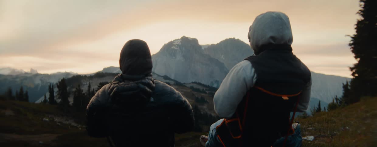 Two male hikers sit in chairs and admire the majestic mountain view from their campsite at sunset