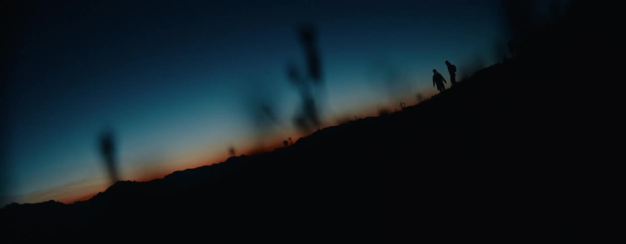 Silhouettes of two hikers with headlamps ascend a mountain trail during the beautiful twilight hour