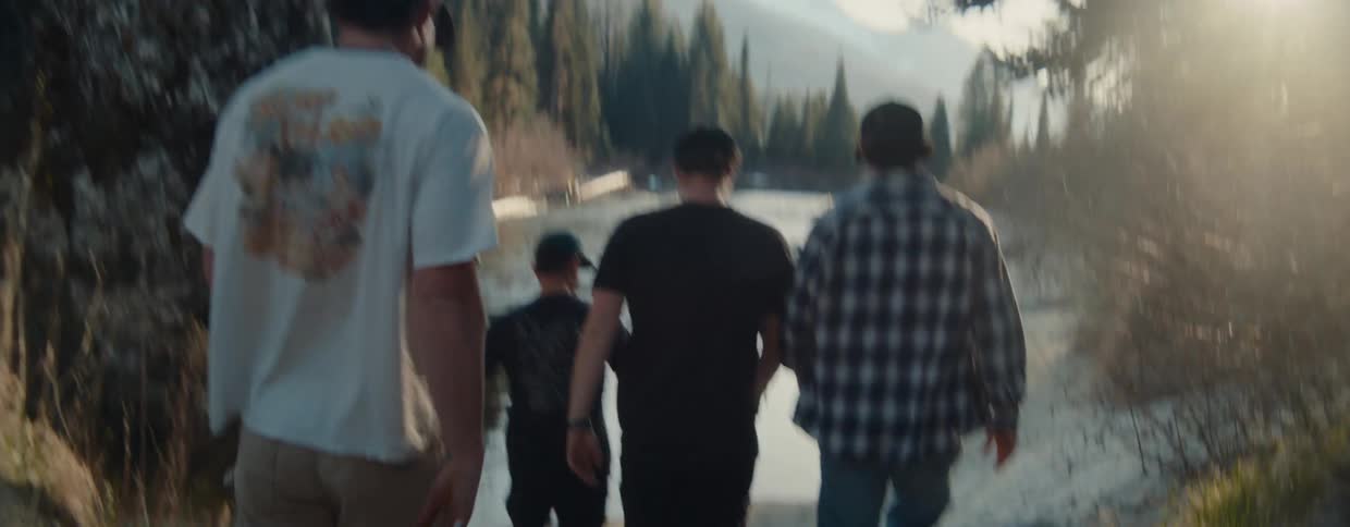 A group of friends walk together to a river's edge in the mountains and share a moment of camaraderie at sunset