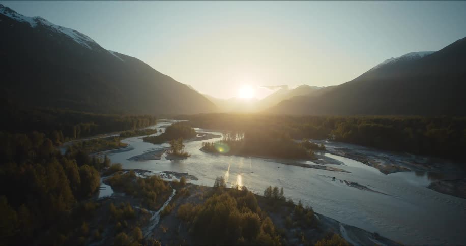 Majestic aerial pull-back shot of a vast river valley and snow-capped mountains during a golden sunset