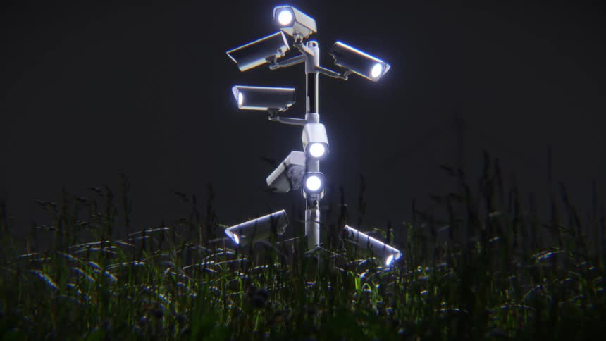 A pole covered in glowing CCTV security cameras stands ominously in a grassy field at night, symbolizing total surveillance