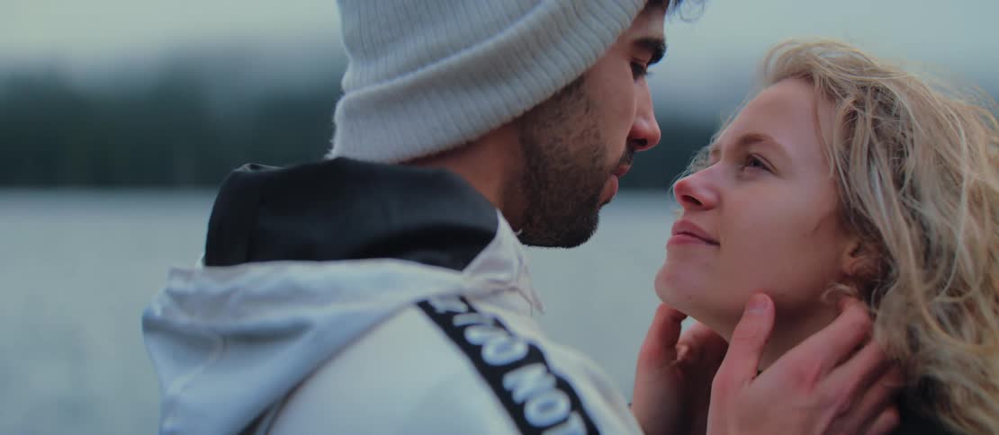 A young couple in love shares a tender, intimate moment, looking into each other's eyes and embracing on a cool, overcast day