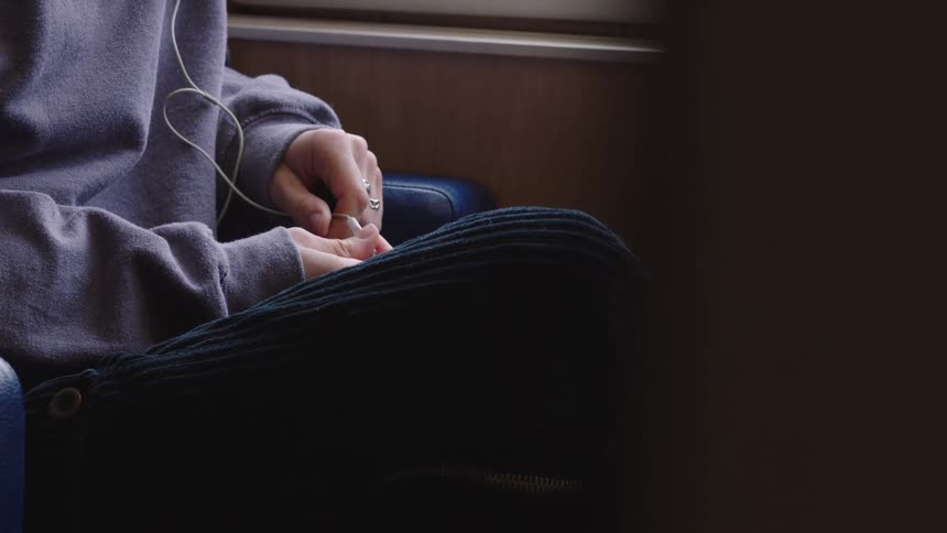 A close-up of a person's hands as they fidget with an earphone cord while traveling on a train