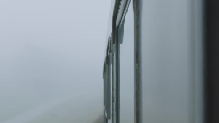 A point-of-view shot from a moving vehicle shows a guardrail passing by on a bridge enveloped in thick, mysterious fog